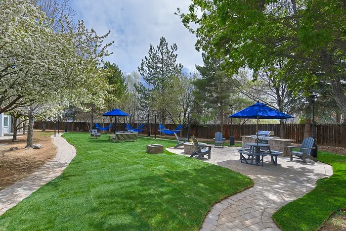 Charming outdoor space with lush green lawns, blue umbrellas, hammocks, and a cozy seating area, perfect for relaxation and gatherings.