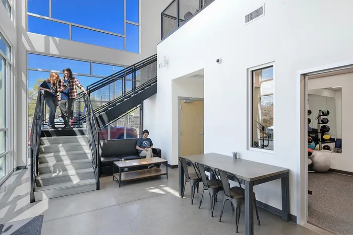 Bright and modern communal living area with high ceilings, chic staircase, and gym access, perfect for social gatherings.