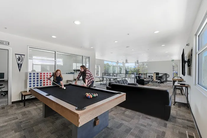 Vibrant community lounge featuring a pool table, cozy seating, and expansive windows with scenic views, perfect for relaxation and entertainment.