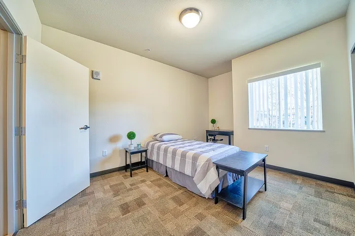 Inviting bedroom with modern decor, cozy single bed, and ample natural light through large windows.