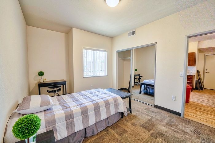 Inviting bedroom with modern decor, featuring a cozy bed, mirrored closets, and a sleek workstation bathed in natural light.