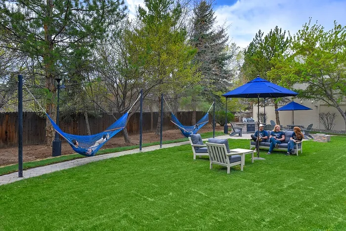Inviting outdoor space featuring lush green lawn, hammocks for relaxation, and seating area with blue umbrellas, perfect for social gatherings.