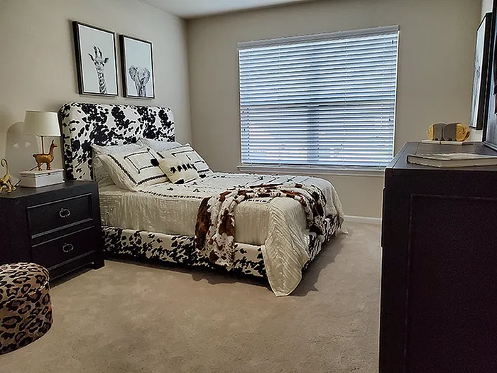 Chic bedroom featuring a cow-print bed frame, elegant decor, and abundant natural light through large window blinds.