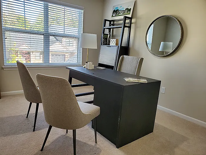 Elegant home office with natural light, featuring a sleek desk, comfortable beige chairs, and modern decor.