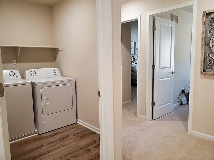 Charming apartment hallway with in-unit washer and dryer, leading to cozy carpeted bedrooms.