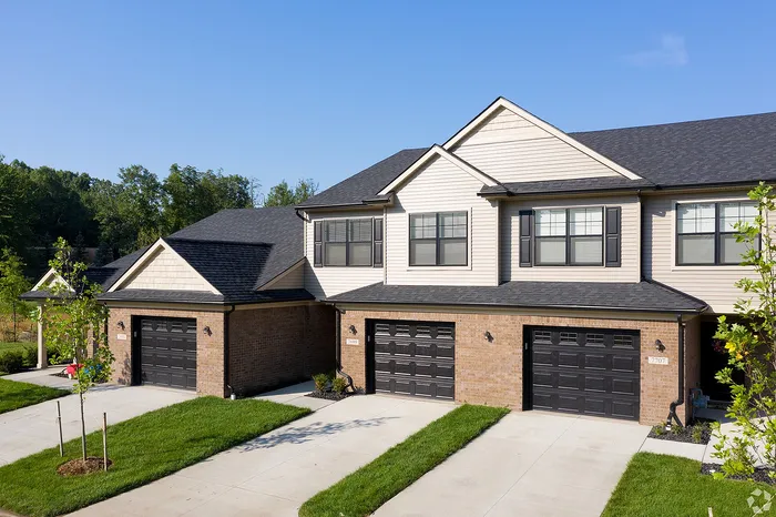 Charming townhouse duo with modern brick facade and sleek black garage doors, set in a lush green neighborhood.