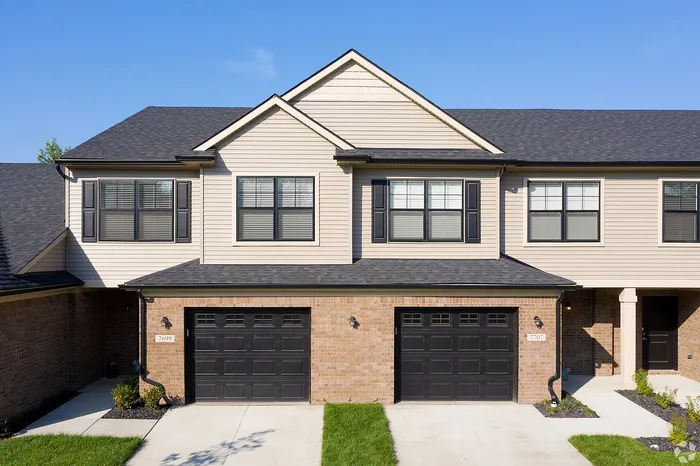 Charming townhouse exterior showcasing modern design with two-car garage, elegant brickwork, and pristine landscaping under a clear blue sky.