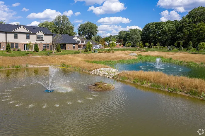 Charming lakeside view with elegant townhomes and vibrant fountains surrounded by lush greenery.