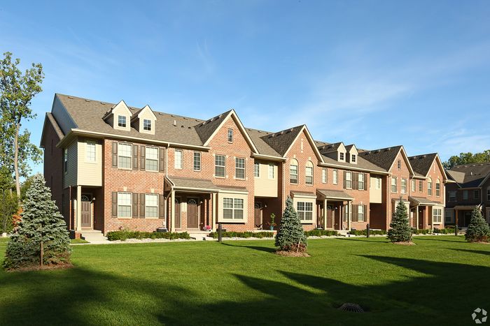 Charming row of brick townhouses with manicured lawns and bright blue sky, perfect for family living.
