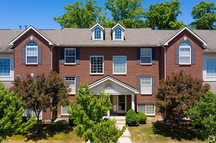 Charming brick townhouse with dormer windows, abundant natural light, surrounded by lush green trees.