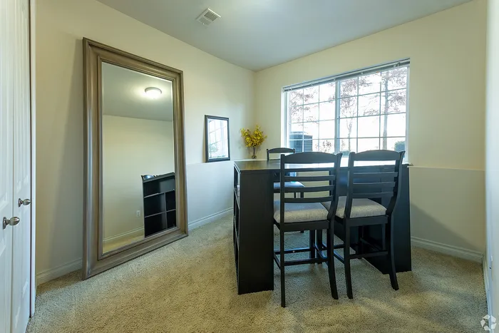 Bright and cozy dining area with a large mirror enhancing space, featuring elegant black furniture and a sunlit window view.