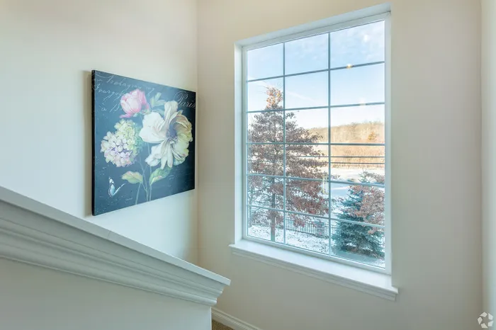 Bright stairwell with large window view and elegant floral artwork, offering a touch of nature indoors.