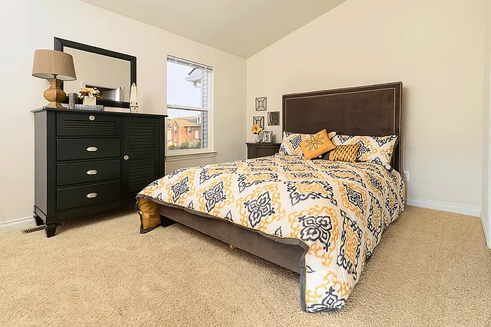 Inviting bedroom with plush carpeting, vibrant bedding, sleek dark dresser, and a large window offering natural light.