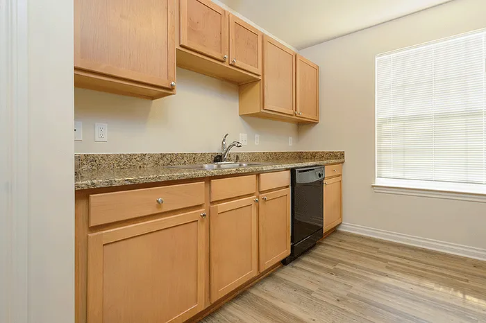 Spacious kitchen with sleek wooden cabinets, modern countertops, and ample natural light through a large window.