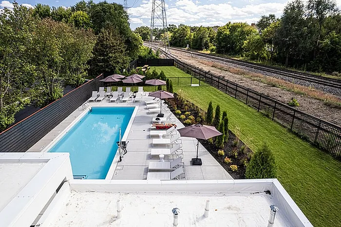 Chic apartment complex with a stylish outdoor pool, sun loungers, and umbrellas surrounded by lush greenery and open spaces.