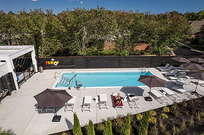 Luxurious outdoor pool area with modern lounge chairs and umbrellas, surrounded by lush greenery, perfect for relaxation and summer enjoyment.