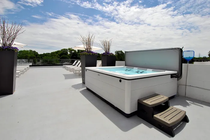 Luxurious rooftop terrace featuring a modern hot tub, elegant sun loungers, and lush greenery under a vibrant sky.
