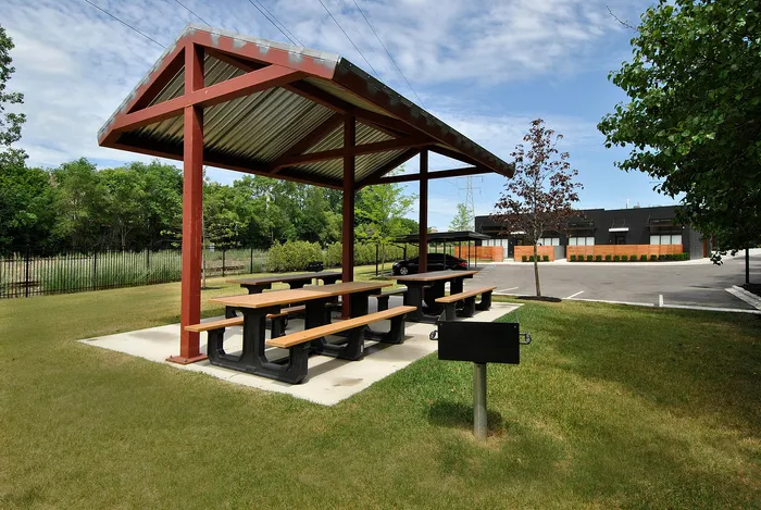 Charming outdoor picnic area with a covered seating space and a barbecue grill, surrounded by lush greenery, ideal for gatherings.