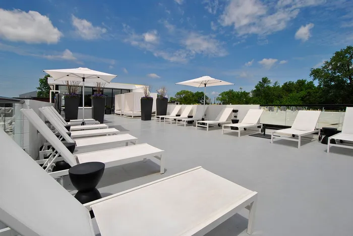 Elegant rooftop terrace with modern lounge chairs and parasols, offering a serene outdoor relaxation space with lush greenery and open skies.