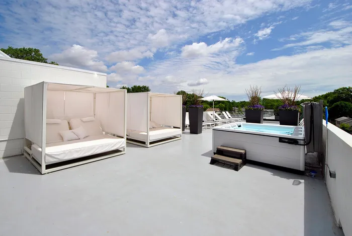 Luxurious rooftop terrace featuring stylish cabanas, a sleek hot tub, and elegant lounge chairs under a bright blue sky.