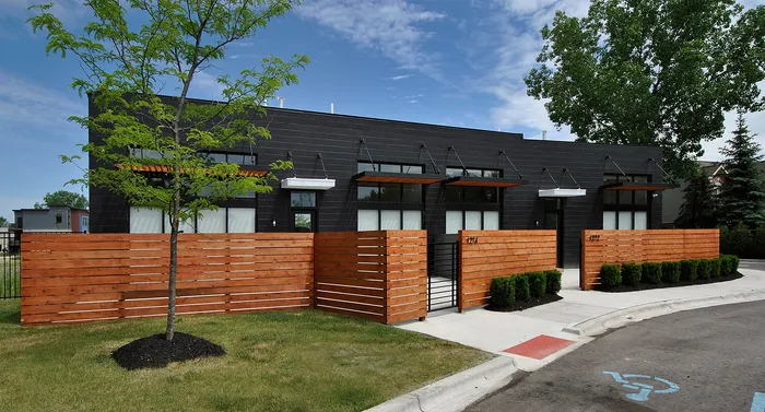 Modern townhouse with sleek black exterior, wooden privacy fence, and lush landscaping, nestled in a serene suburban setting.
