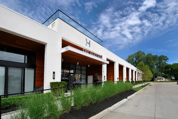 Modern building exterior of The Harrison, featuring sleek architecture with glass railings and lush landscaping against a blue sky backdrop.