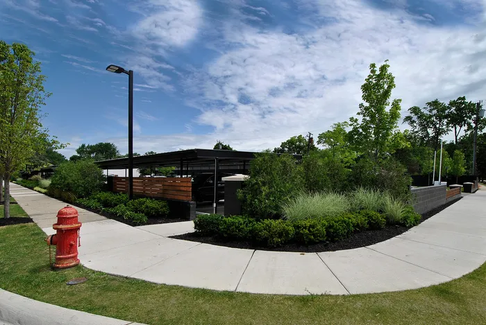Inviting neighborhood view with lush greenery, modern carport, and picturesque sidewalk under a clear blue sky.
