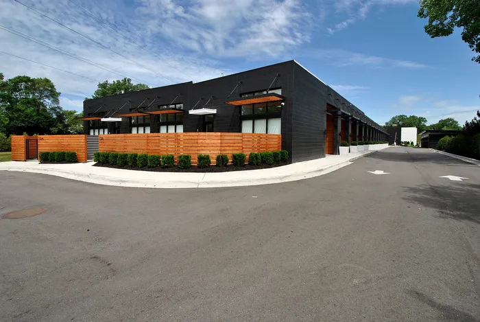 Modern industrial building featuring sleek black facade with decorative wooden accents and neatly landscaped greenery on a spacious lot.