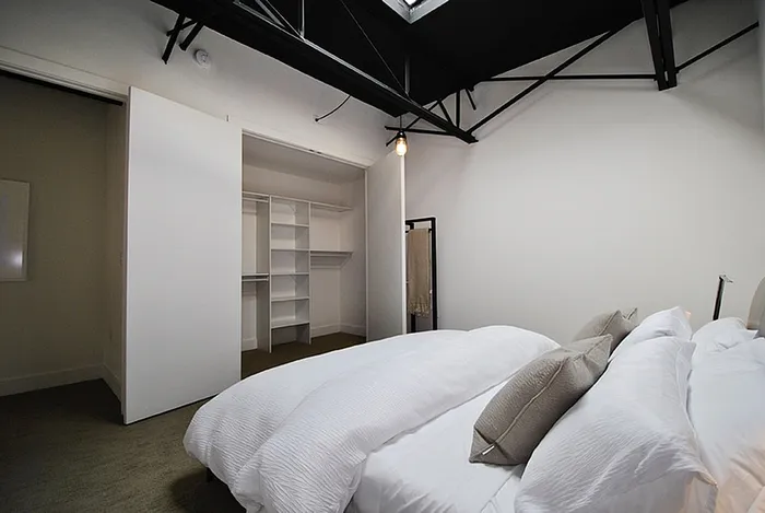 Modern bedroom with skylight, white bedding, and spacious walk-in closet for an airy and inviting atmosphere.