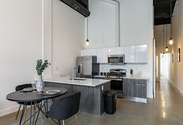 Modern kitchen and dining area with sleek appliances, elegant black table and chairs, and stylish pendant lighting in a spacious apartment.
