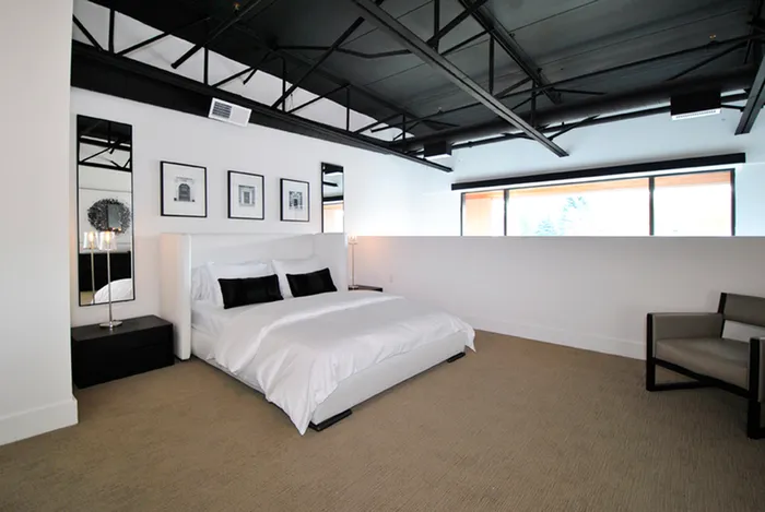 Modern industrial-style bedroom featuring sleek black ceiling beams, elegant wall art, and luxurious bedding, creating a chic and comfortable retreat.