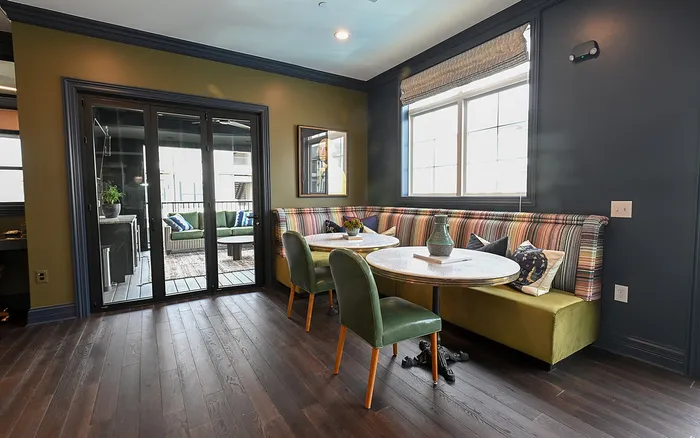 Chic apartment dining area with elegant green chairs, colorful cushioned bench seating, and a view of the cozy outdoor patio through large glass doors.
