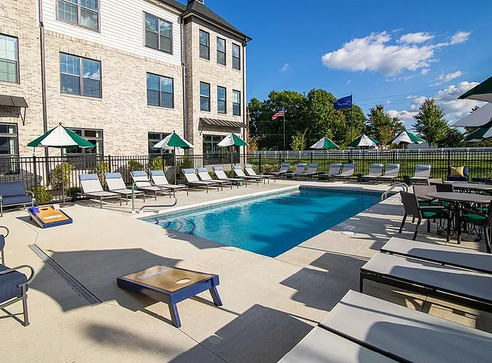 Luxurious apartment complex with a sparkling outdoor pool, surrounded by stylish lounge chairs and vibrant green umbrellas, perfect for relaxation and leisure.