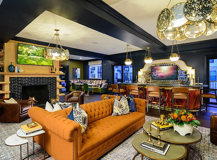Luxurious apartment lounge with elegant lighting, plush orange sofa, cozy fireplace, and stylish bar area.