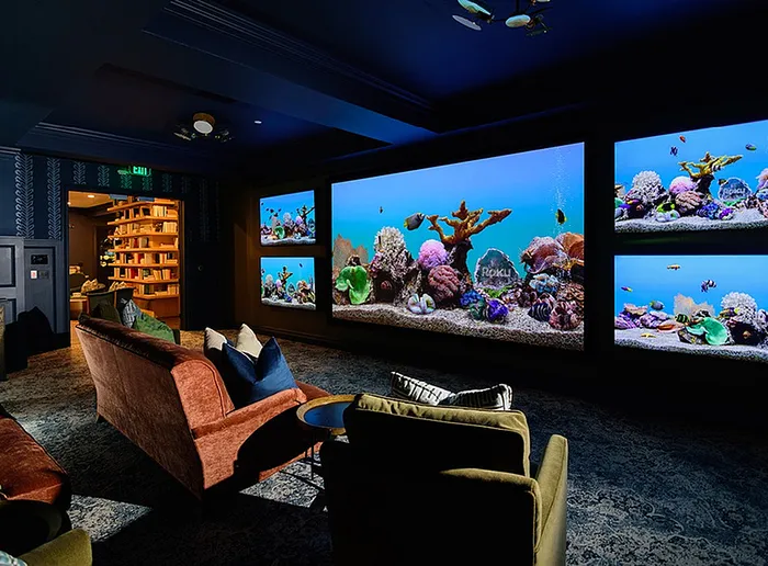 Luxury home theater with plush seating, featuring an impressive wall of vibrant aquariums illuminating the room.