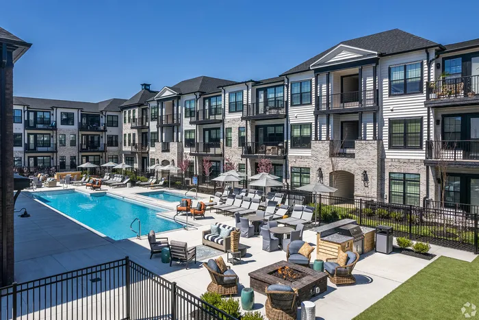 Luxurious apartment complex with modern three-story buildings surrounds a sparkling outdoor swimming pool, featuring cozy lounge areas and a stylish fire pit.