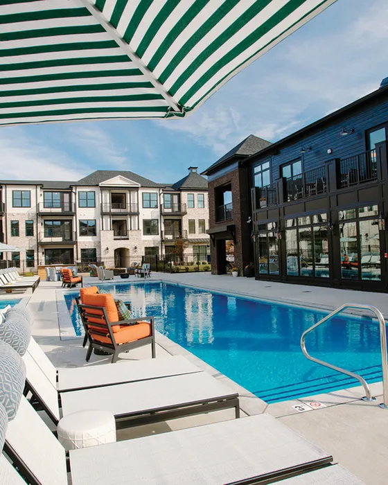Luxurious poolside view showcasing modern apartment complex with elegant architecture and inviting lounge chairs under striped umbrellas.