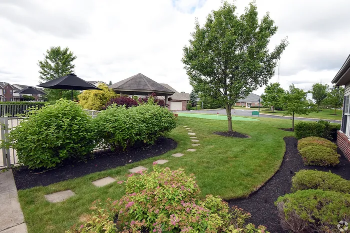 Lush landscaped garden with a scenic pathway, vibrant greenery, and cozy gazebo under a cloudy sky, offering serene outdoor living.