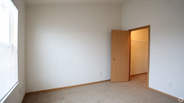 Bright bedroom with plush carpet and a walk-in closet, featuring elegant wood trim and ample natural light from large windows.