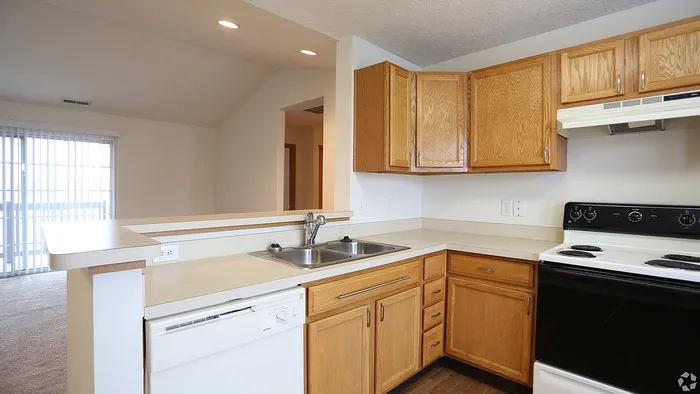 Bright and inviting kitchen with modern appliances, wooden cabinetry, and a breakfast bar leading to a spacious living area with natural light.