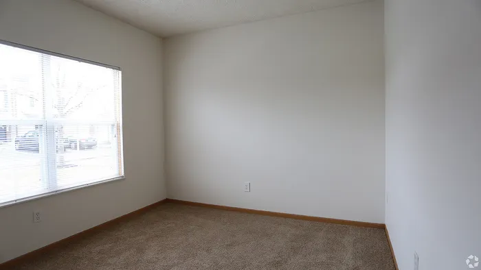 Bright and airy corner of a cozy room with large window, soft carpet, and clean white walls, perfect for a personalized touch.