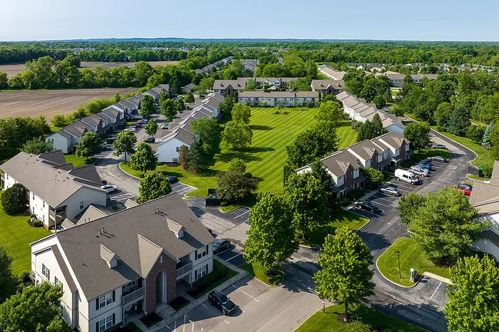 Charming aerial view of a picturesque apartment community surrounded by lush greenery and spacious lawns, offering tranquil suburban living.