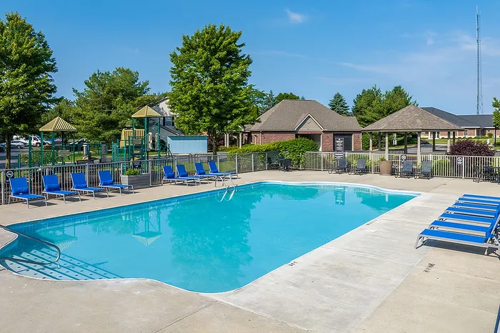 Inviting apartment complex pool with vibrant blue lounge chairs and a nearby playground, offering a perfect family-friendly leisure setting.