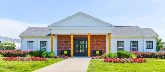 Charming apartment building entrance with a vibrant flower garden, welcoming benches, and classic brick facade.