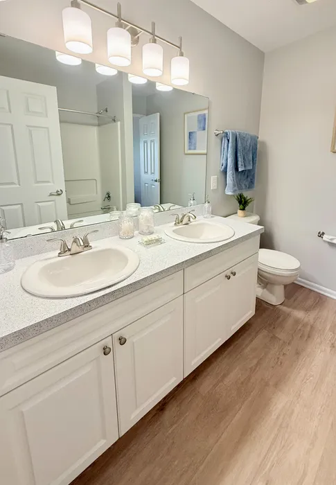 Bright and modern bathroom with dual sinks, elegant quartz countertops, and warm wood flooring.