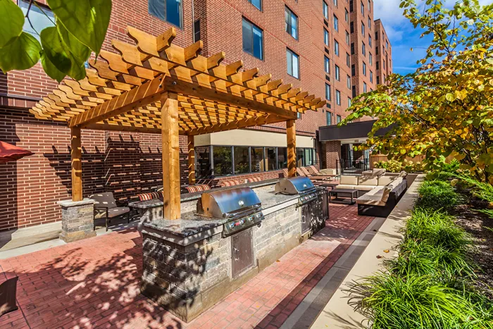 Inviting outdoor patio with modern grills and cozy seating under a charming wooden pergola, perfect for hosting gatherings.