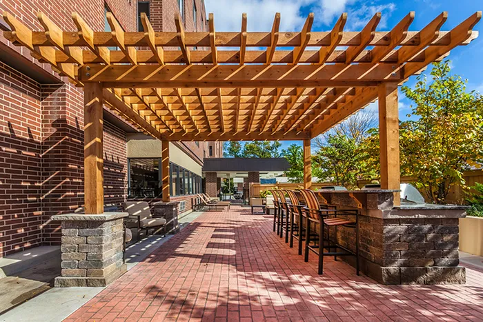 Chic outdoor patio with wooden pergola, cozy seating, and modern barstools under a vibrant blue sky.