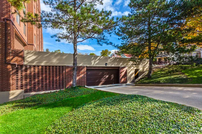 Charming apartment exterior with elegant brickwork, lush greenery, and a serene driveway under a bright blue sky.