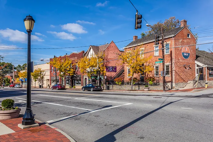 Charming urban street view featuring historic brick buildings, vibrant autumn foliage, and a clear blue sky.