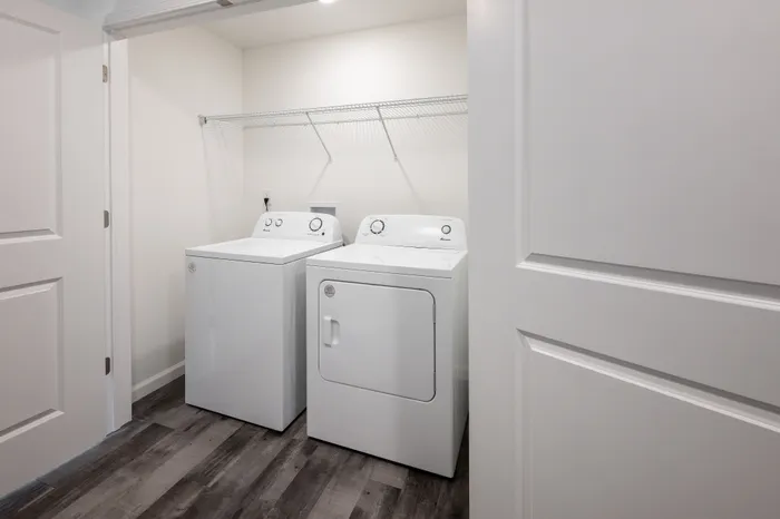 Modern laundry room with sleek white washer and dryer units, set against elegant hardwood flooring and minimalistic shelving.